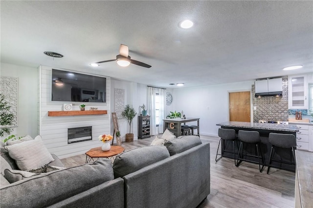 living room with a textured ceiling, ceiling fan, a fireplace, and light hardwood / wood-style flooring