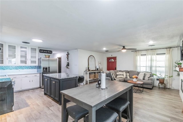 kitchen with ceiling fan, a kitchen island, stainless steel refrigerator with ice dispenser, white cabinets, and light wood-type flooring