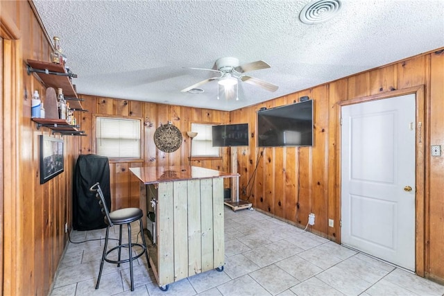 kitchen featuring kitchen peninsula, a textured ceiling, ceiling fan, wooden walls, and a breakfast bar area