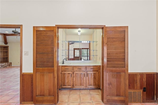 bar with ceiling fan, sink, beamed ceiling, wood walls, and light tile patterned floors