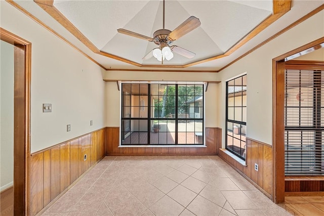 empty room with a tray ceiling, ceiling fan, crown molding, and wood walls