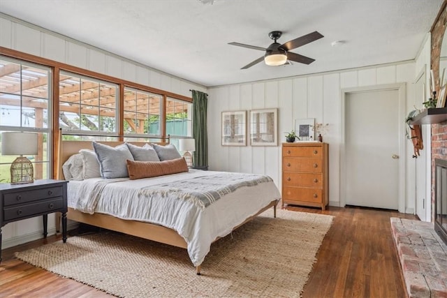 bedroom with hardwood / wood-style floors, ceiling fan, crown molding, and a brick fireplace