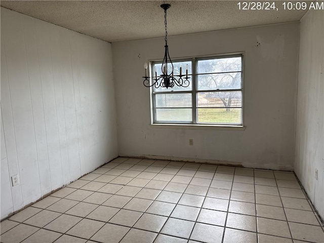 unfurnished dining area with light tile patterned floors, wood walls, an inviting chandelier, and a textured ceiling