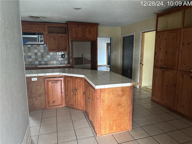 kitchen with kitchen peninsula, tile counters, decorative backsplash, light tile patterned flooring, and a textured ceiling