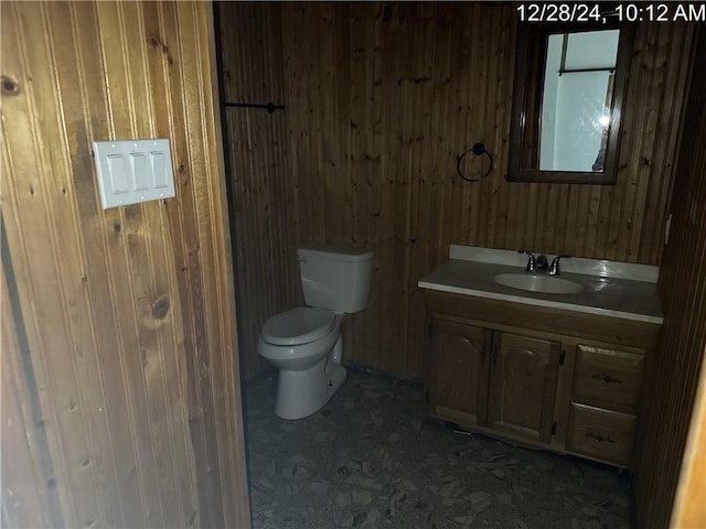 bathroom with toilet, wood walls, and vanity