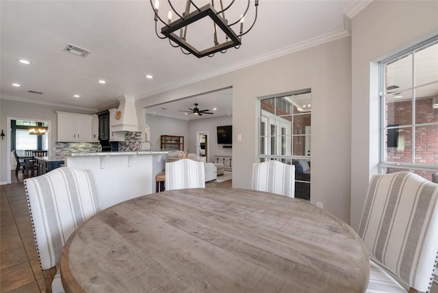 tiled dining room with a healthy amount of sunlight, ceiling fan with notable chandelier, and ornamental molding