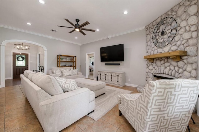 living room with ceiling fan with notable chandelier, a stone fireplace, ornamental molding, and light tile patterned floors