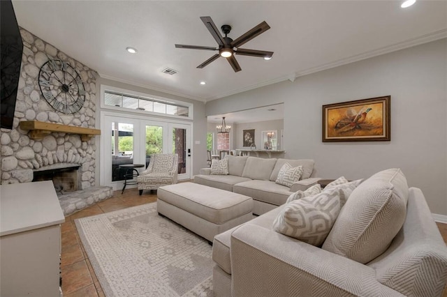 living room with ceiling fan with notable chandelier, a stone fireplace, ornamental molding, and light tile patterned flooring