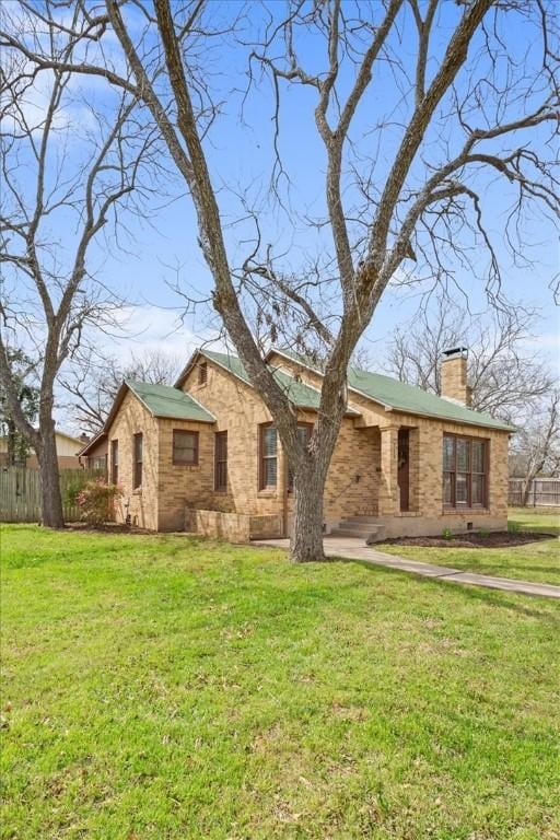 view of front facade featuring a chimney, a front yard, and fence