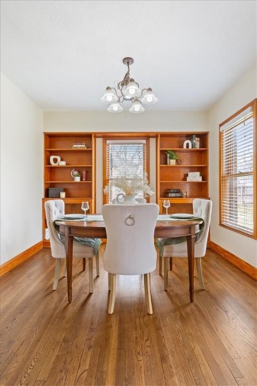 dining area with built in features, baseboards, wood-type flooring, and a chandelier