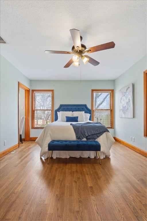 bedroom featuring baseboards, multiple windows, a textured ceiling, and light wood finished floors