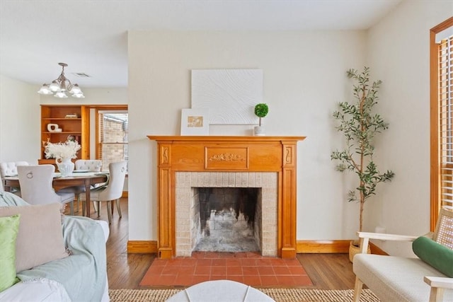 living area featuring visible vents, baseboards, a chandelier, a fireplace, and wood finished floors