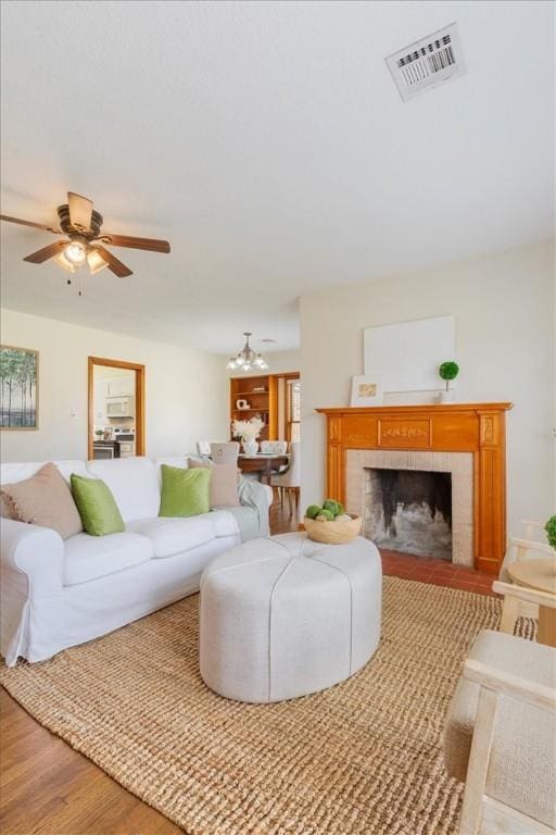 living room featuring visible vents, a fireplace, a ceiling fan, and wood finished floors