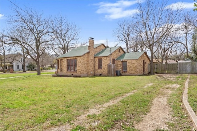 view of side of property with brick siding, a lawn, a chimney, and fence