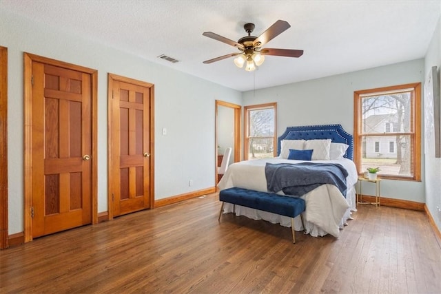 bedroom with multiple windows, wood finished floors, visible vents, and baseboards