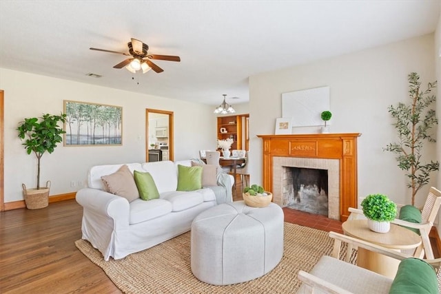 living room featuring visible vents, baseboards, ceiling fan with notable chandelier, a fireplace, and wood finished floors