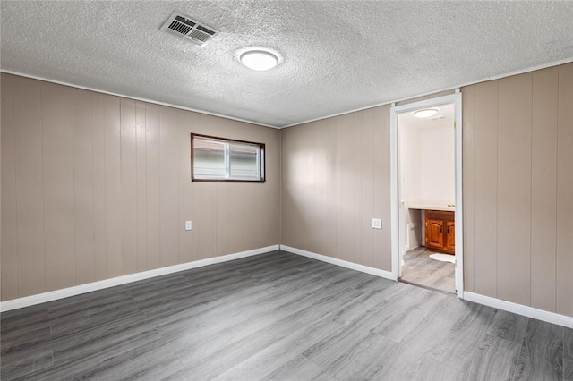 spare room with a textured ceiling, light wood-type flooring, and wooden walls