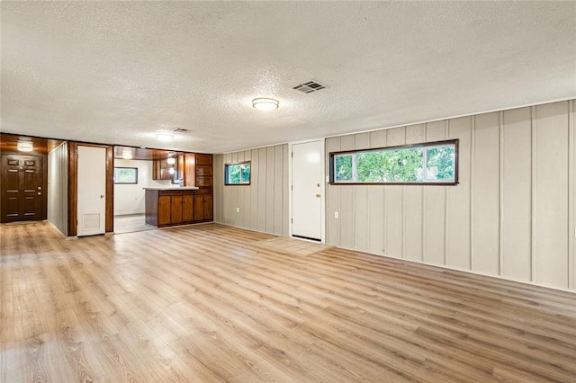 unfurnished living room featuring a textured ceiling, light hardwood / wood-style flooring, and wooden walls