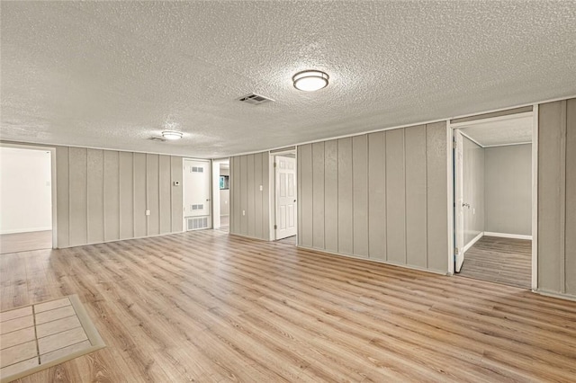 interior space with a textured ceiling, light wood-type flooring, and wood walls