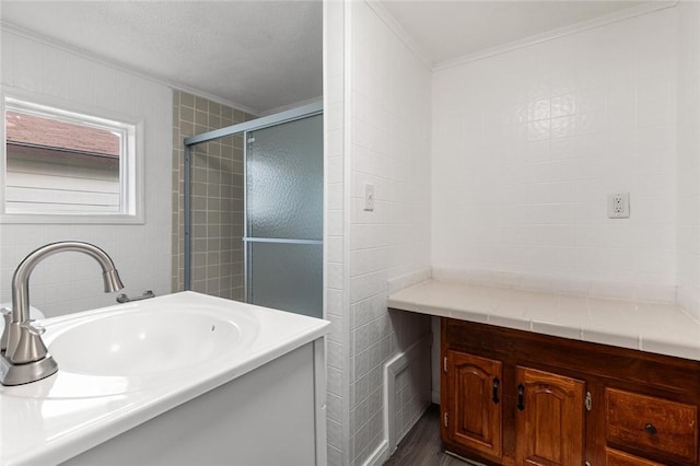 bathroom featuring a textured ceiling, vanity, a shower with shower door, tile walls, and ornamental molding