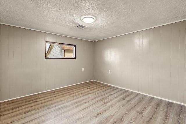 unfurnished room with wood walls, light hardwood / wood-style floors, and a textured ceiling