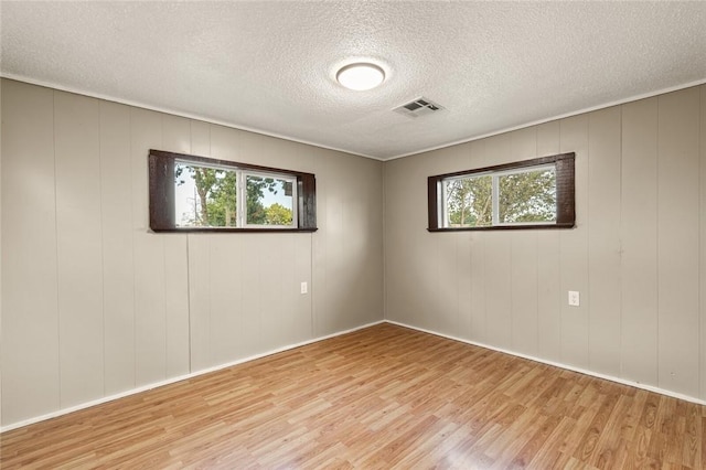 spare room featuring light hardwood / wood-style floors, a textured ceiling, and wooden walls