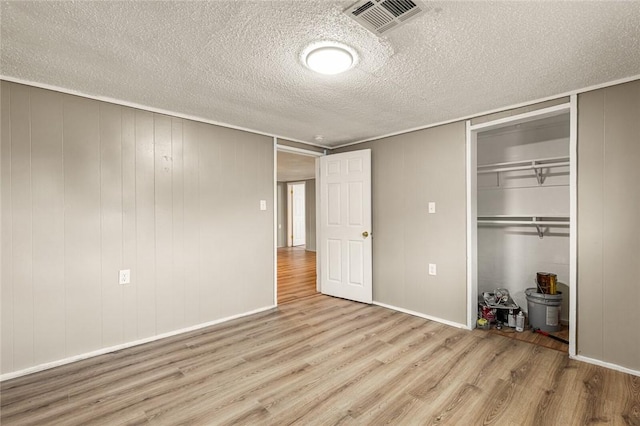 unfurnished bedroom featuring a textured ceiling, light hardwood / wood-style floors, a closet, and wood walls