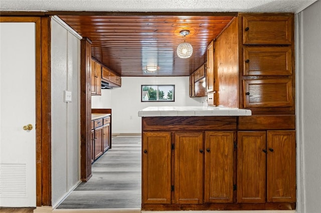 kitchen with kitchen peninsula, tile counters, light hardwood / wood-style flooring, and decorative light fixtures