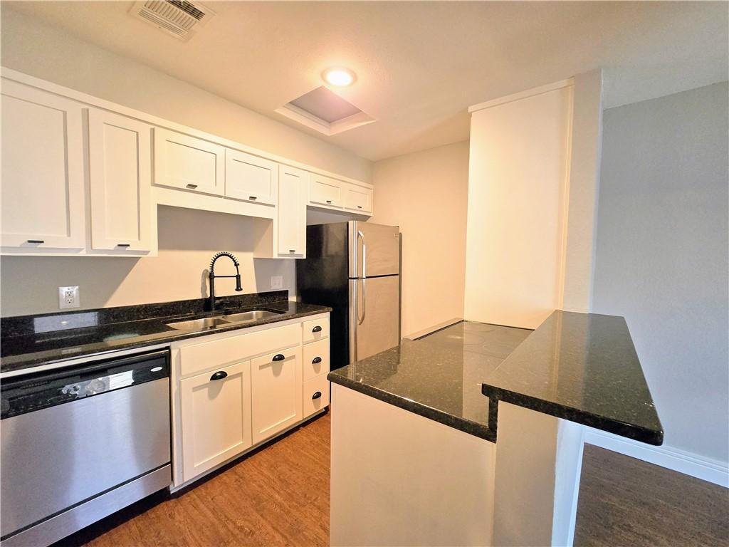 kitchen featuring white cabinetry, sink, light hardwood / wood-style flooring, dark stone countertops, and appliances with stainless steel finishes