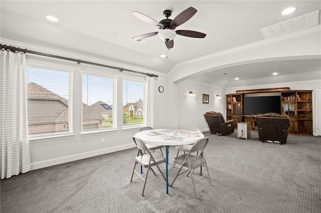 carpeted dining room with arched walkways, vaulted ceiling, baseboards, and crown molding