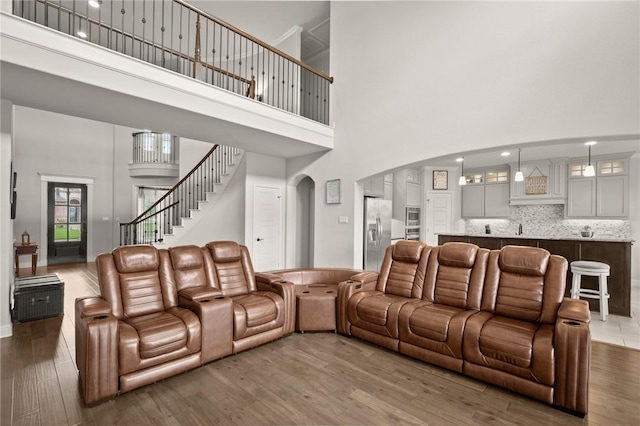 living area with dark wood-type flooring, arched walkways, a towering ceiling, and stairs