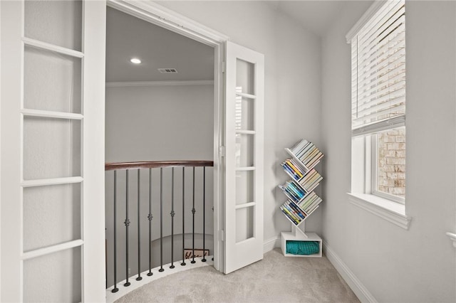 hallway with carpet flooring, crown molding, visible vents, and baseboards