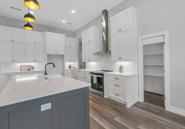 kitchen featuring stainless steel range with electric stovetop, wall chimney exhaust hood, sink, decorative light fixtures, and white cabinetry