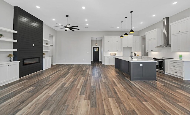 kitchen with stainless steel stove, white cabinetry, a center island with sink, and wall chimney range hood