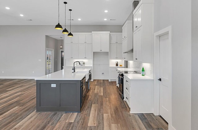 kitchen with pendant lighting, dark wood-type flooring, white cabinets, a center island with sink, and electric stove