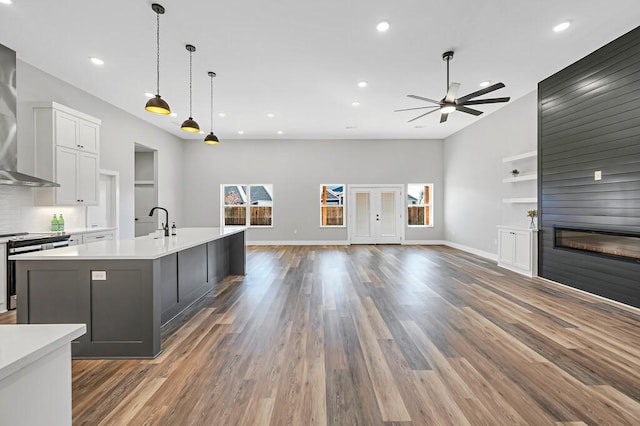 kitchen with pendant lighting, a center island with sink, ceiling fan, a large fireplace, and dark hardwood / wood-style flooring