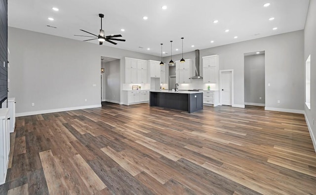 kitchen with a center island with sink, wall chimney exhaust hood, dark hardwood / wood-style floors, decorative light fixtures, and a large fireplace