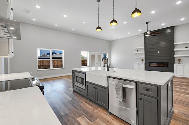 kitchen with appliances with stainless steel finishes, a large fireplace, hanging light fixtures, and gray cabinetry