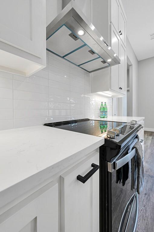 kitchen featuring decorative backsplash, ventilation hood, white cabinetry, and hardwood / wood-style flooring