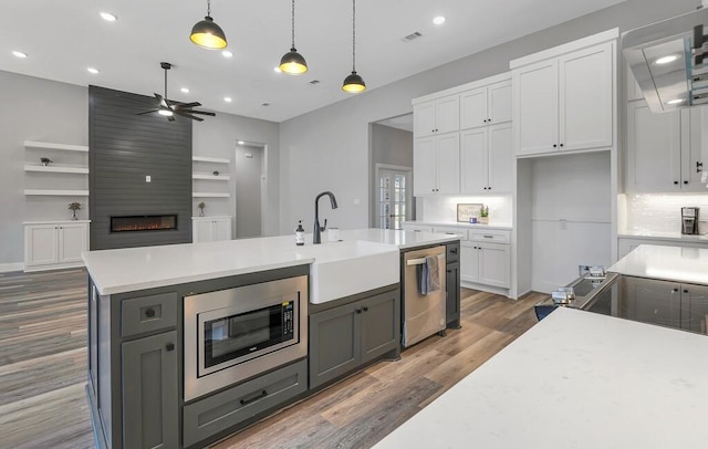 kitchen featuring a large fireplace, stainless steel appliances, sink, white cabinetry, and hanging light fixtures