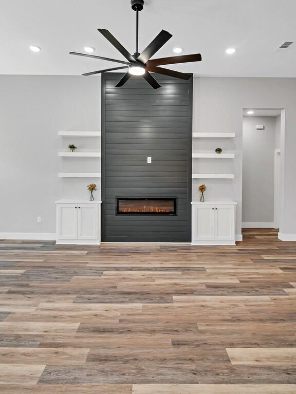 unfurnished living room with ceiling fan, a large fireplace, built in features, and light hardwood / wood-style flooring