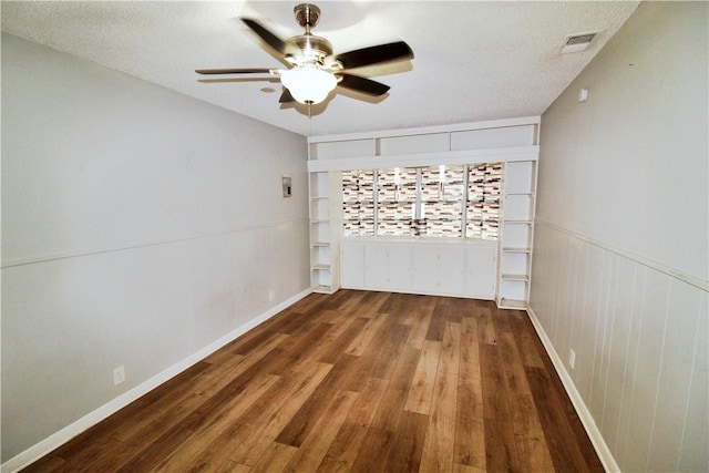 spare room featuring a textured ceiling, ceiling fan, wood walls, and dark wood-type flooring