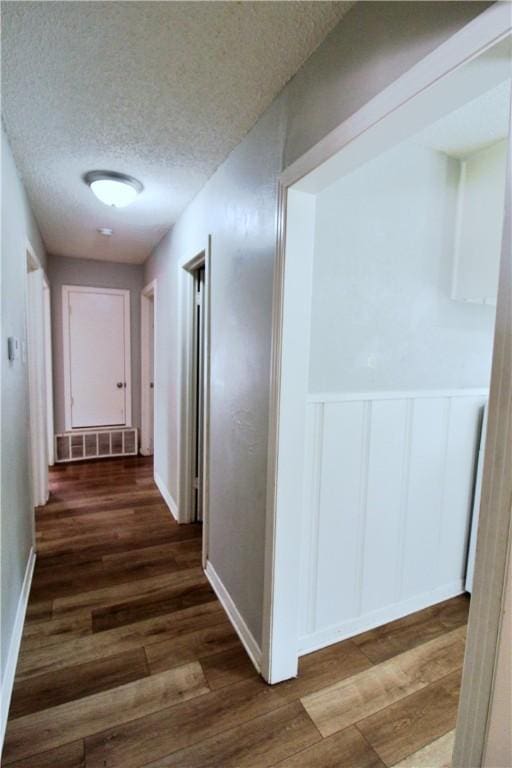 corridor with a textured ceiling and dark wood-type flooring