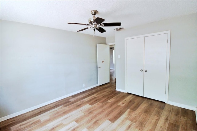 unfurnished bedroom featuring a textured ceiling, a closet, light hardwood / wood-style flooring, and ceiling fan