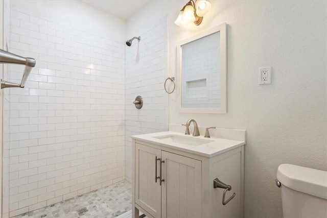 bathroom featuring a tile shower, vanity, and toilet