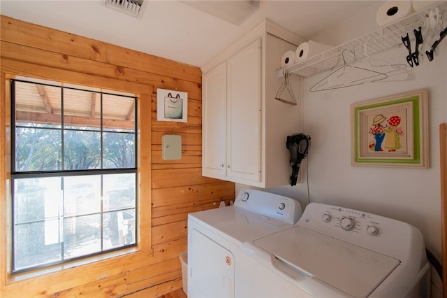 clothes washing area featuring cabinets, independent washer and dryer, and wooden walls