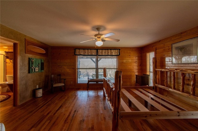 interior space featuring ensuite bathroom, wood walls, ceiling fan, and dark hardwood / wood-style floors