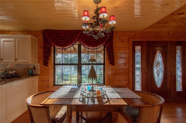 dining area featuring hardwood / wood-style floors, wood walls, wooden ceiling, and an inviting chandelier