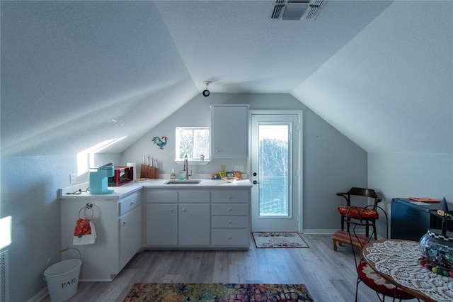 kitchen featuring white cabinets, light wood-type flooring, vaulted ceiling, and sink