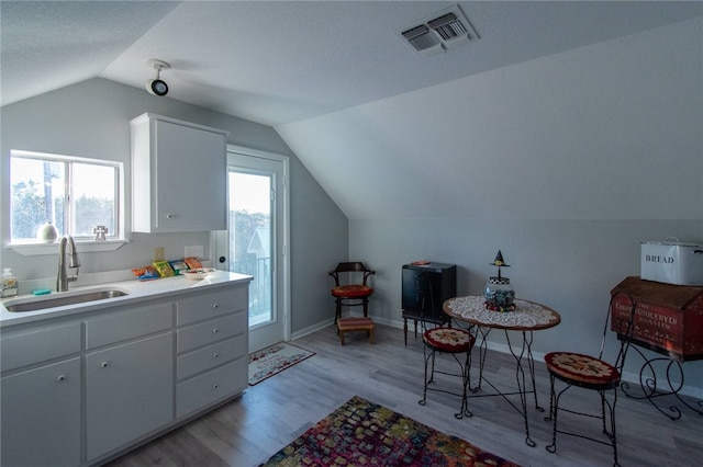 kitchen featuring light wood-type flooring, vaulted ceiling, white cabinetry, and sink